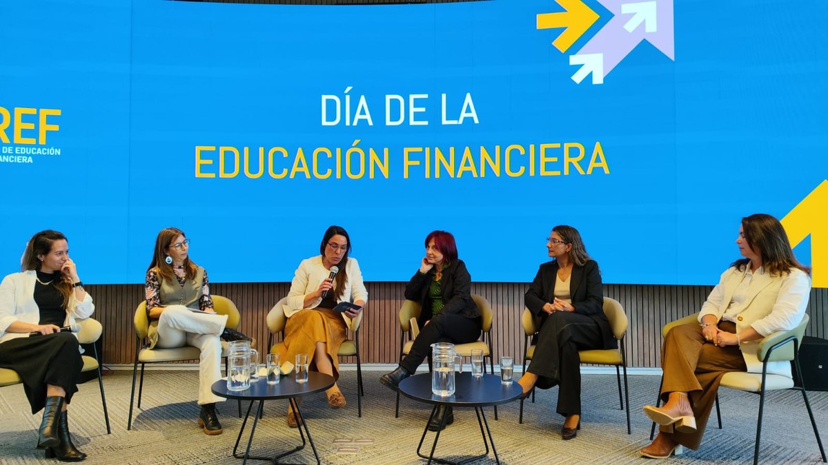 Seis panelistas sentadas en el escenario, frente a una pantalla azul con el texto Día de la Educación Financiera, en el encuentro anual de la Red de Educación Financiera
